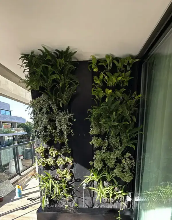 Jardín vertical denso en un balcón con puerta vidriada