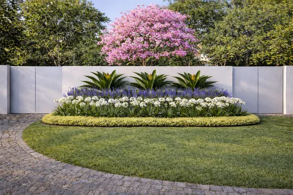 Render de un cantero circular con agapantos y flores blancas, con un árbol en flor rosada detrás